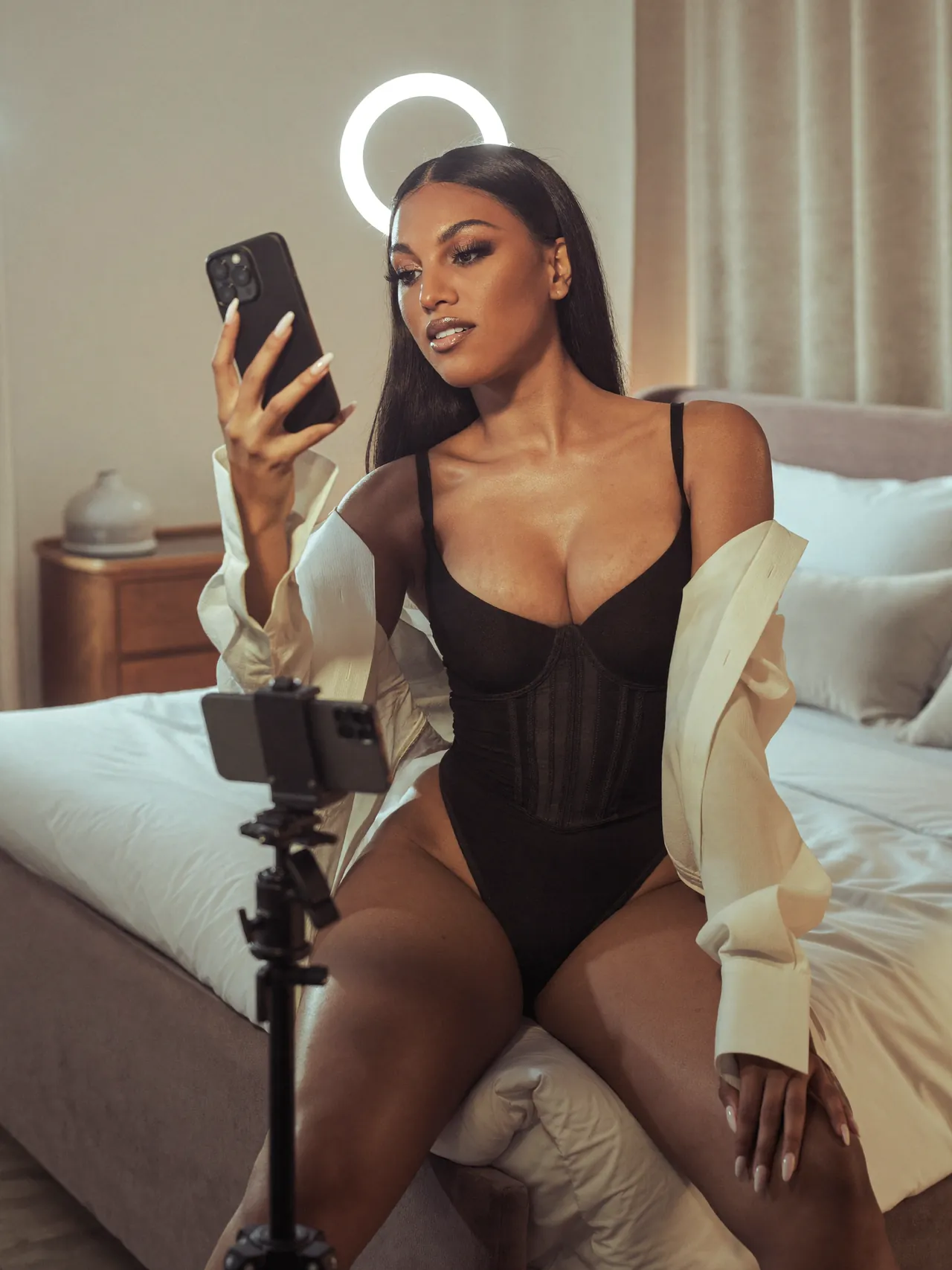 Une créatrice vérifie son téléphone sur un trépied, anneau lumineux allumé, dans sa chambre studio.